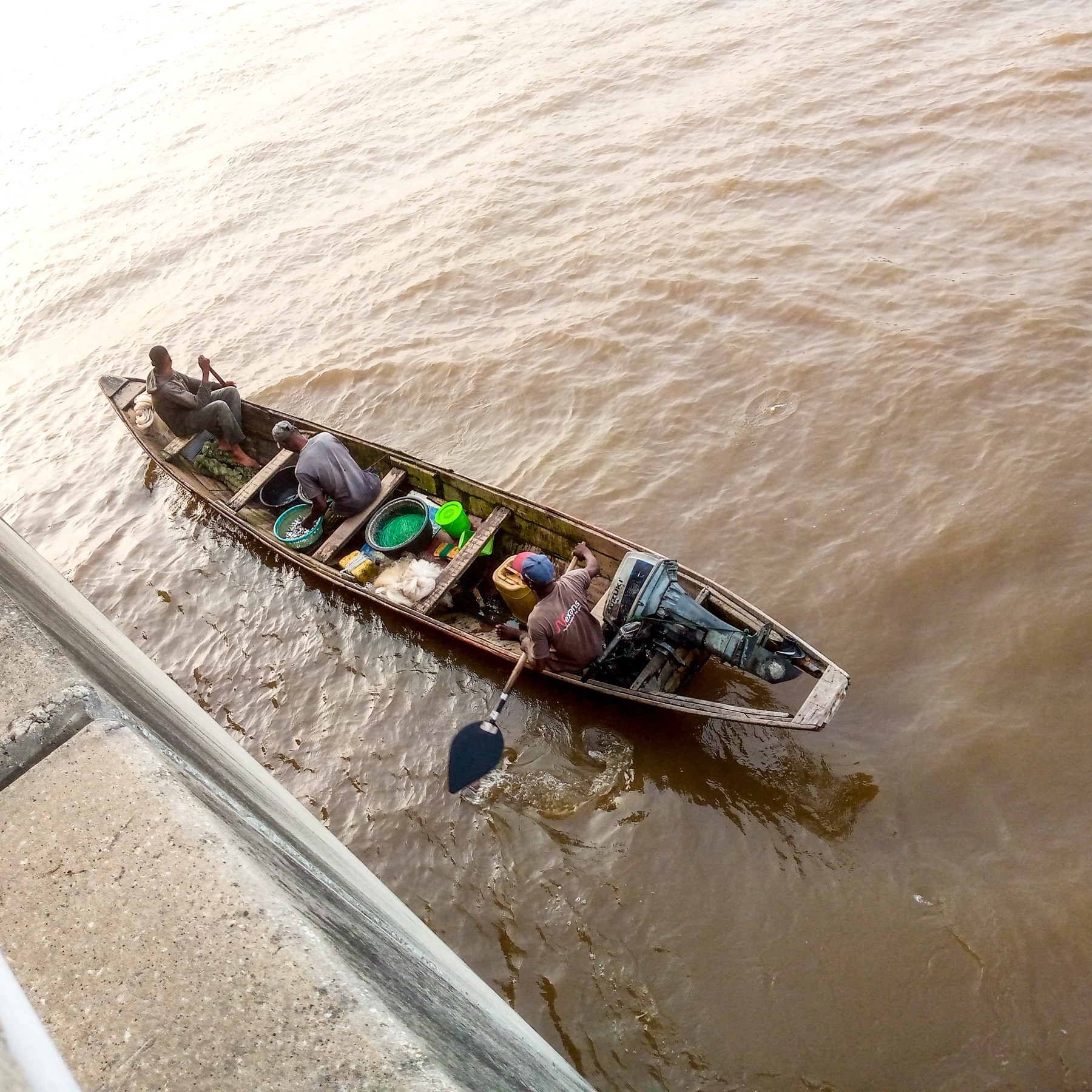 Three fishermen in a wooden boat with nets and an outboard engine on a Nigerian river