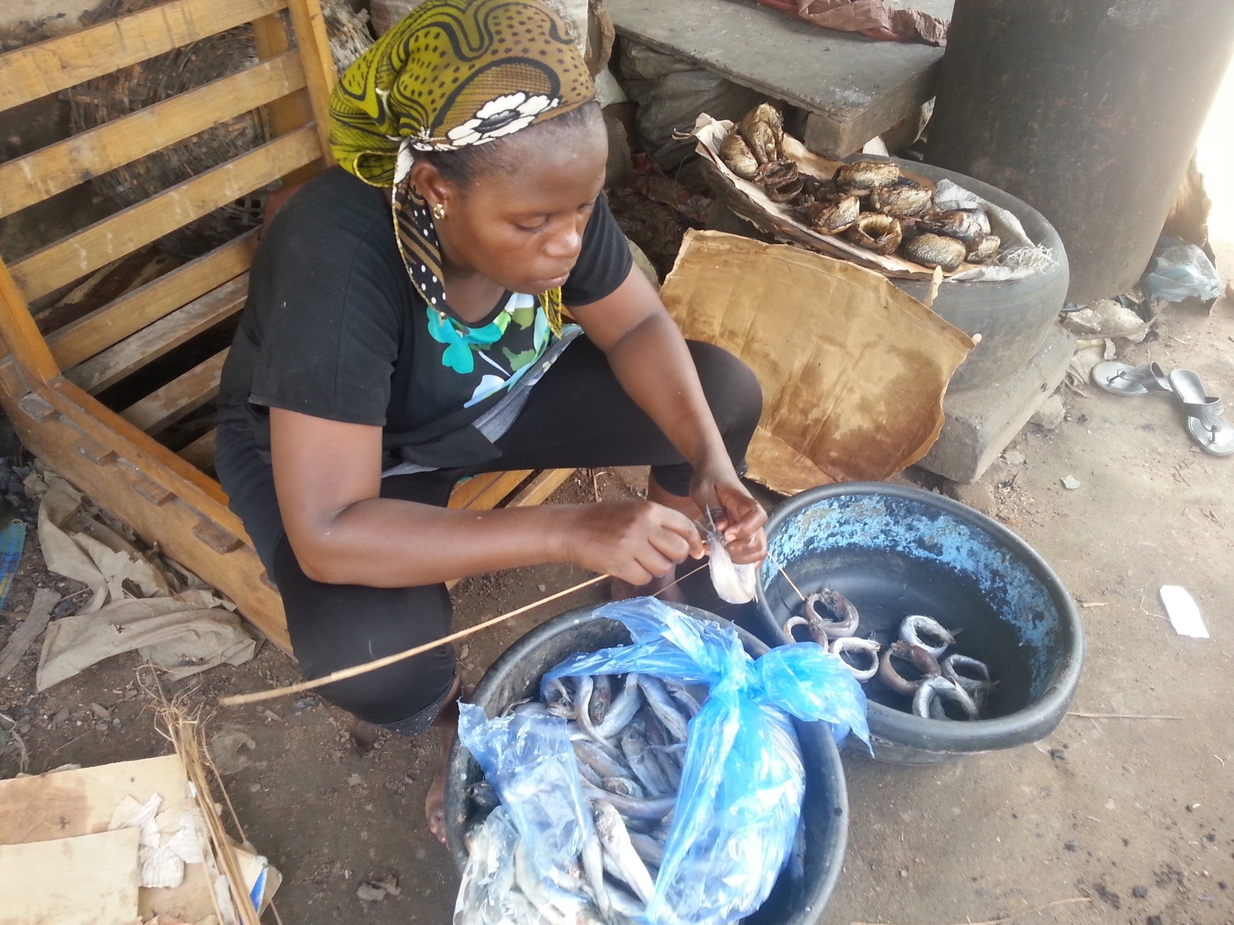 A woman dressing fresh fish beside smoked fish in Nigeria