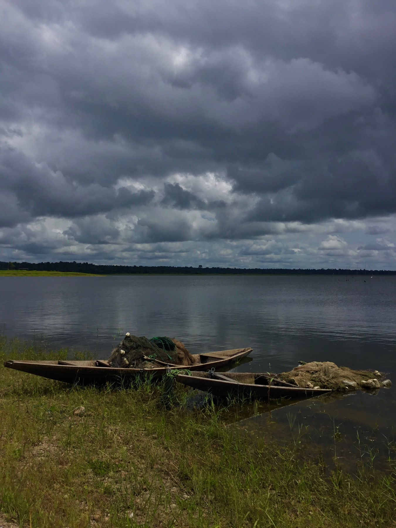 Two wooden fishing canoes with nets pulled up on a Nigerian lakeshore